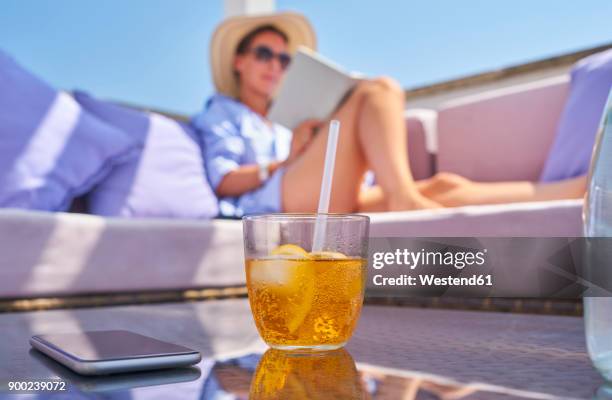 glass of crodino, smartphone and woman relaxing on sun deck in background - woman ice stock-fotos und bilder