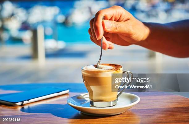 close-up of woman's hand stirring glass of espresso macchiato - espresso drink stock pictures, royalty-free photos & images