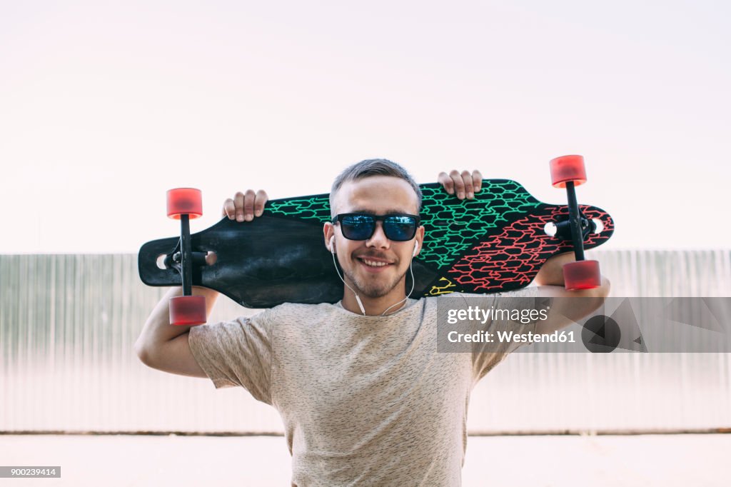 Portrait of confident young man with earbuds carrying longboard