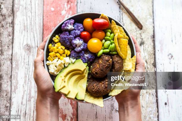 girl's hands holding quinoa veggie bowl of vegetables, feta, nachos and quinoa fritters - veggie burger stock pictures, royalty-free photos & images