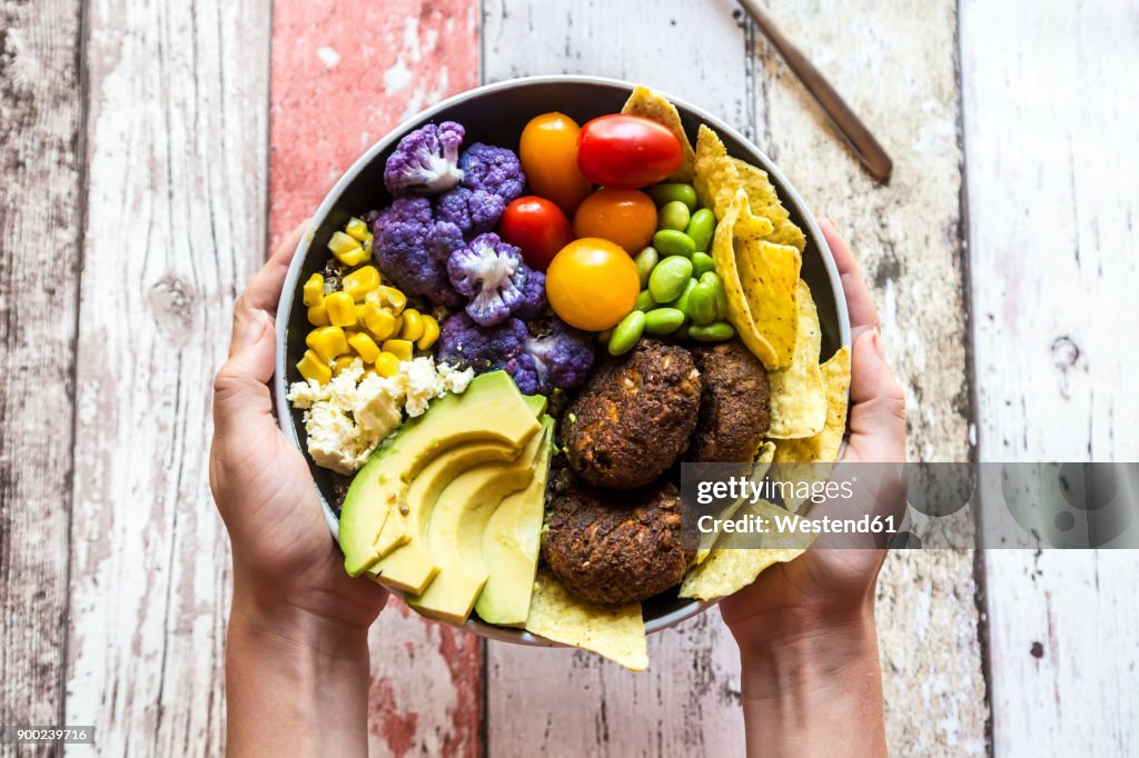 Girl's hands holding Quinoa veggie bowl of vegetables, feta, nachos and quinoa fritters
