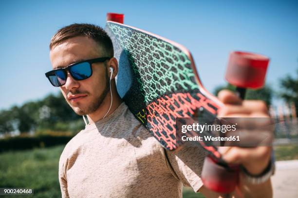 young man with earbuds carrying longboard - surfar com prancha longa imagens e fotografias de stock