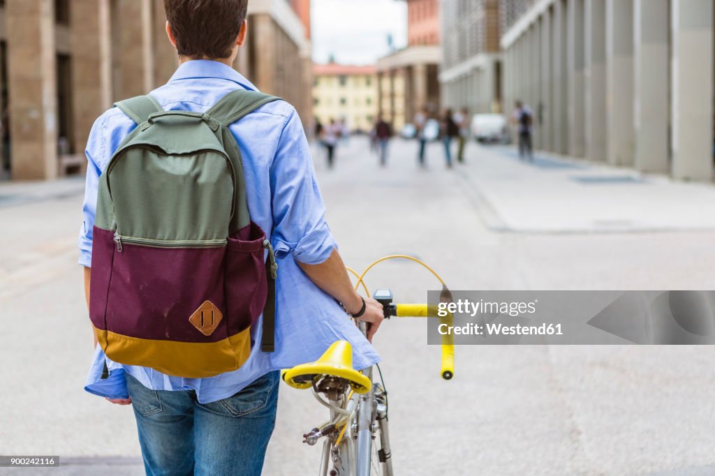 Back view of young man with backpack pushing his bike