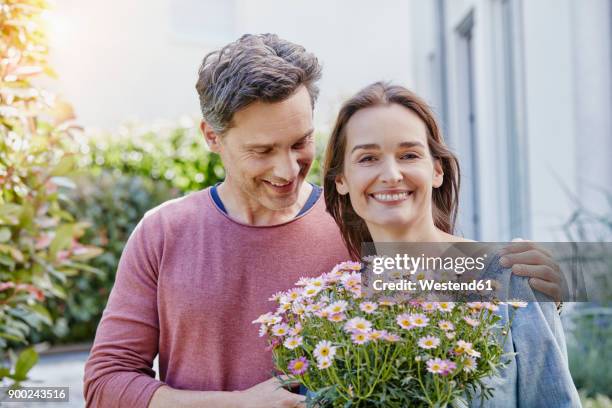 portrait of smiling couple with flowers in front of their home - gift bag stock pictures, royalty-free photos & images