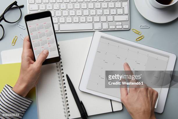 top view of woman holding smartphone and tablet with calendar on desk - calendario foto e immagini stock