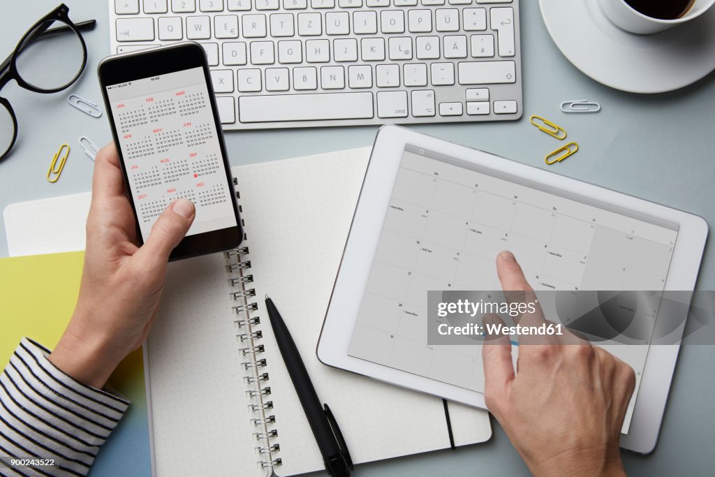 Top view of woman holding smartphone and tablet with calendar on desk