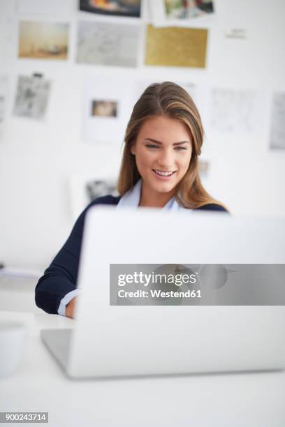 smiling young woman using laptop at desk in office - computer front view stock pictures, royalty-free photos & images