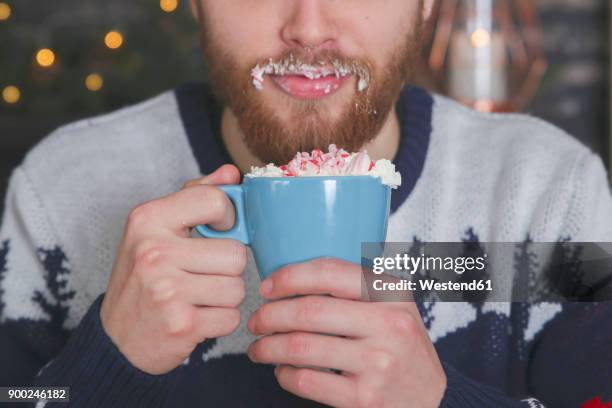 man drinking hot chocolate with whipped cream and chopped candy canes at christmas time - whip stock pictures, royalty-free photos & images