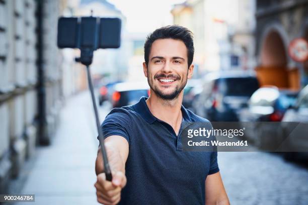 man taking photo with smartphone mounted on selfie stick - selfie stick stock pictures, royalty-free photos & images