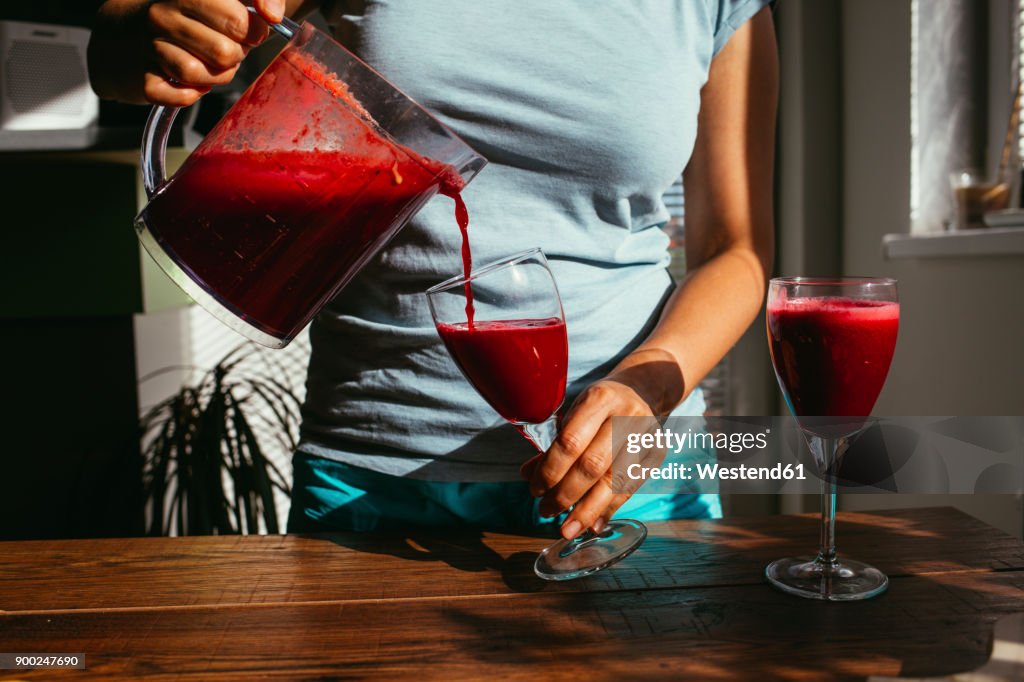 Woman pouring fresh squeezed juice into glasses, partial view