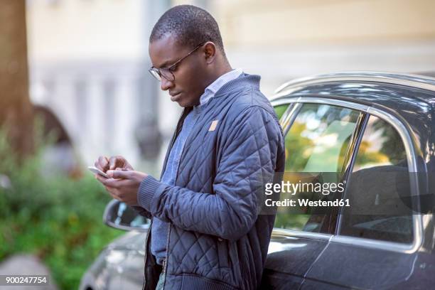 young man leaning against car using cell phone - phone leaning stock pictures, royalty-free photos & images