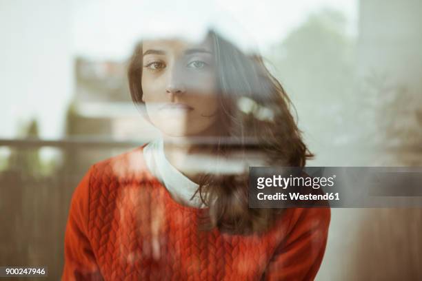 portrait of serious young woman behind glass pane - fenster stock-fotos und bilder