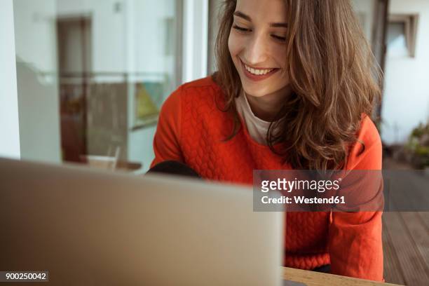 smiling young woman using laptop on balcony - laptop stock-fotos und bilder