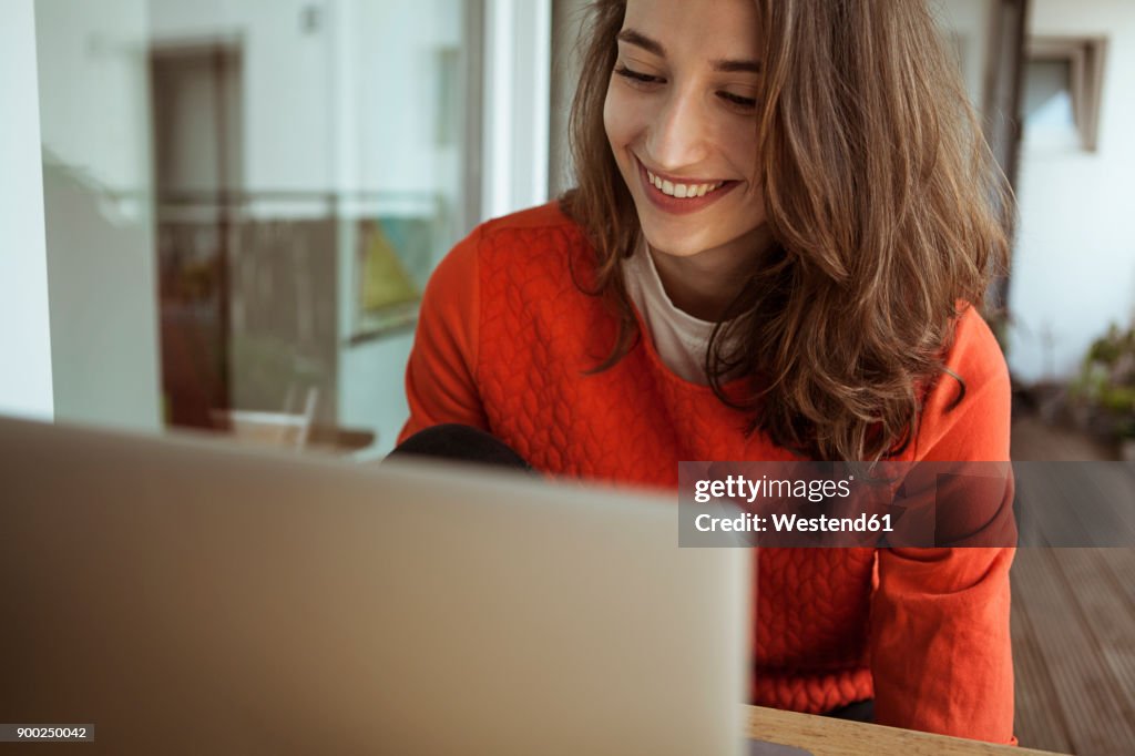 Smiling young woman using laptop on balcony