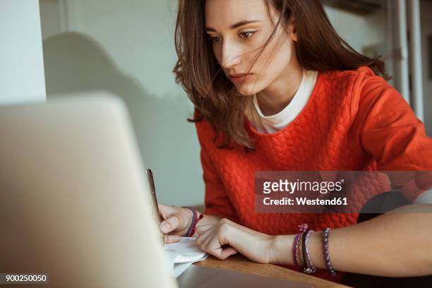young woman working on laptop and papers - konzentration stock-fotos und bilder