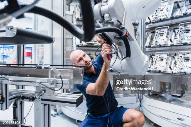 man working at industrial robot in modern factory - robot stock pictures, royalty-free photos & images