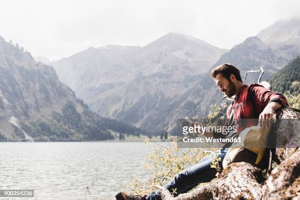 austria, tyrol, alps, hiker relaxing on tree trunk at mountain lake checking cell phone - standing water ストックフォトと画像