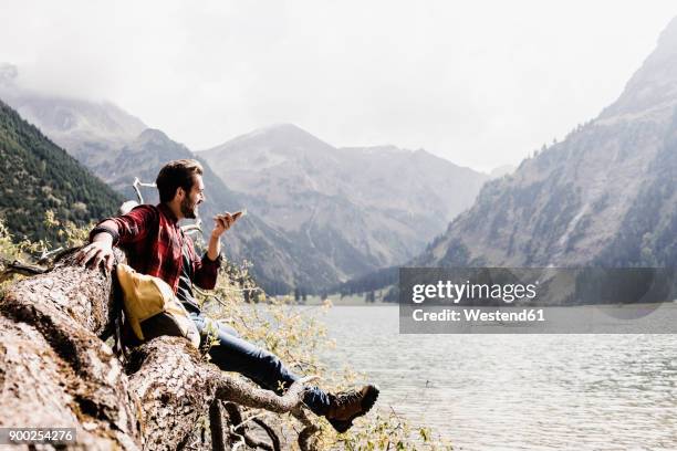 austria, tyrol, alps, hiker on tree trunk at mountain lake using cell phone - mann auf berg mit smartphone stock-fotos und bilder