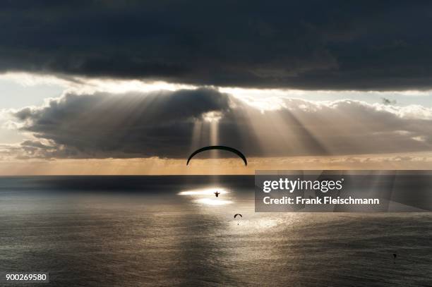 sun shines behind dark clouds with paraglider over the atlantic, puerto naos, canary island of la palma, spain - puerto naos stock pictures, royalty-free photos & images