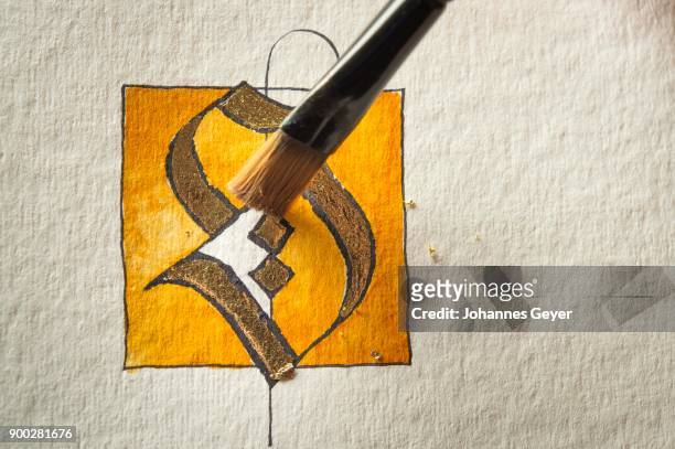 calligraphy studio, paintbrush removing residual transfer gold, letters s coated with gold on torchon paper at back, seebruck, upper bavaria, germany - torchon stock-fotos und bilder