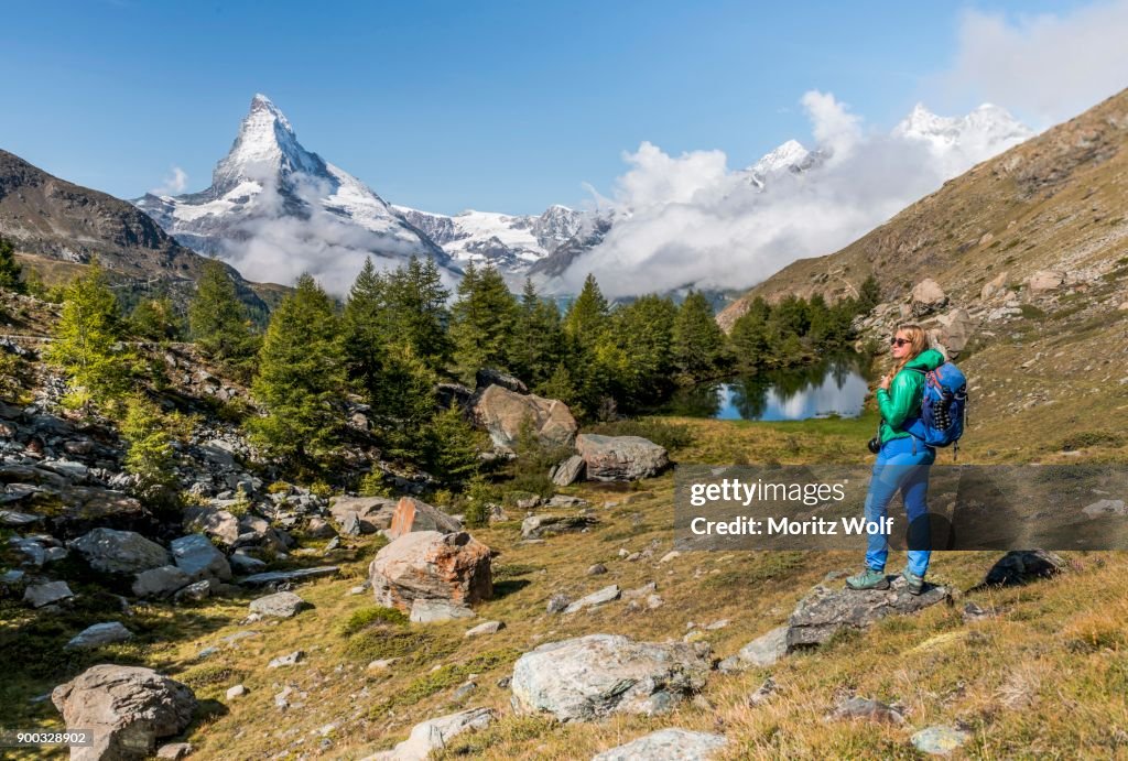 Hiker stands on rocks and looks into the distance, behind Grindijsee and snow-covered Matterhorn, Valais, Switzerland