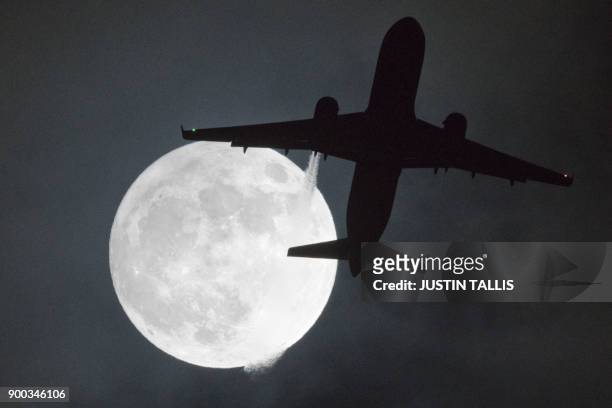 Plane flys in front of a "super moon" or "wolf moon" on its approach to London Heathrow Airport on January 1, 2018. / AFP PHOTO / Justin TALLIS