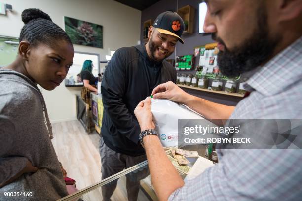 Budtender Danny Buelna shows customers Mariah Roy and Edward Ochoa how to use the required child-proof bag for their purchases at the Green Pearl...