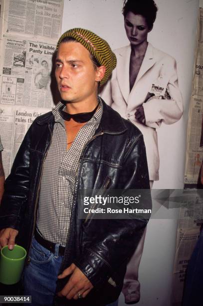 American actor Johnny Depp, dressed in a leather jacket and knit cap with a pair of sunglasses around his neck, stands next to a photograph of his...
