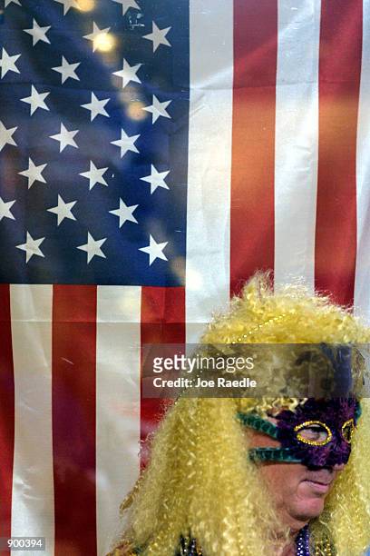 Man dressed in costume stands next to an American flag as he watches a masquerade parade October 27, 2001 during the Key West, Florida Fantasy Fest.