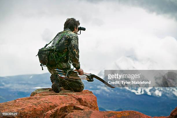 male bow hunter looking through binoculars. - spy hunter stock pictures, royalty-free photos & images