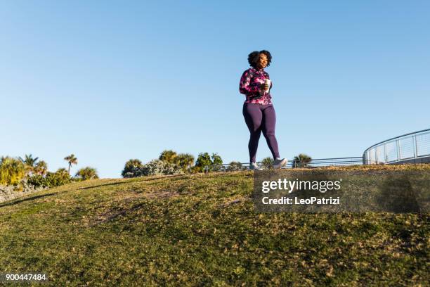 curvilínea jovem negra caminhando, correndo e correndo no parque público da cidade - curvy black women - fotografias e filmes do acervo