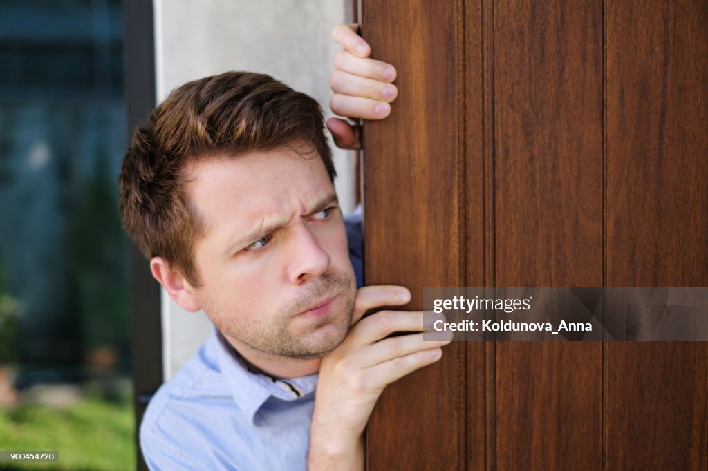 Jeune homme caucasien avec agoraphobie espionnage et regardant dehors la porte.