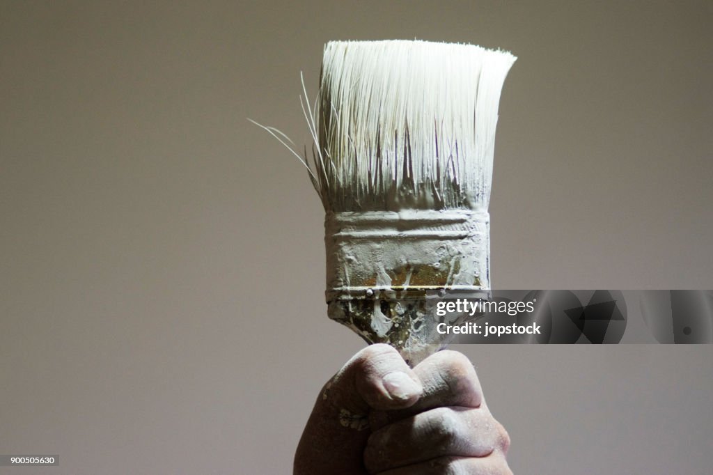 Hand holding a paintbrush with white paint