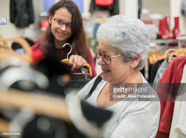 a mulher de sênior ativa de cabelos prateados 65 anos de idade e sua neta adolescente compras em loja de varejo de roupas - 65 69 years - fotografias e filmes do acervo