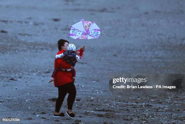 Woman struggles to hold a child and umbrella on Dollymount strand in Dublin as winds start to pick up.