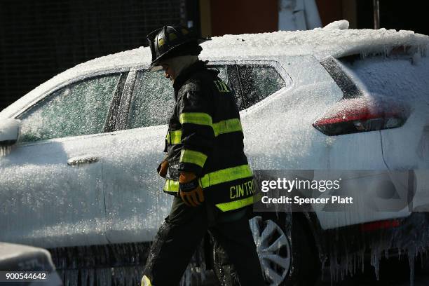 Firefighter walks by an iced over car after fighting a 7-alarm fire on January 2, 2018 in the Bronx borough of New York City. The fire, which started...