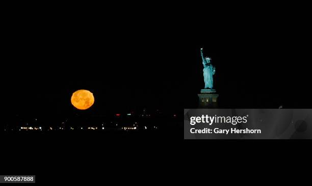 The moon sets next to the Statue of Liberty before sunrise on January 1, 2018 in New York City.