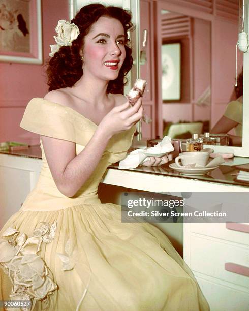 Actress Elizabeth Taylor enjoys tea and a cake in her dressing room, circa 1950.