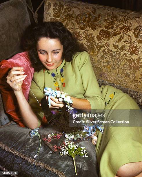 Actress Elizabeth Taylor sewing with artificial flowers, circa 1950.