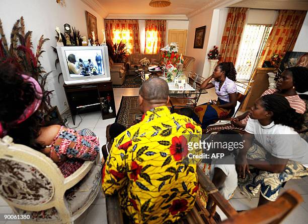 Ivorian actress and director Akissi Delta , flanked by her relatives, watches a TV screen displaying an episode of her former television serie "Ma...