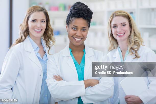 team of confident female pharmacists smiling for photo in neighborhood pharmacy - woman pharmacist stock pictures, royalty-free photos & images