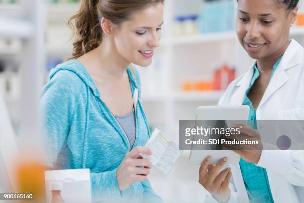 professional pharmacist using digital tablet to assist customer in pharmacy - female pharmacist with a digital tablet imagens e fotografias de stock