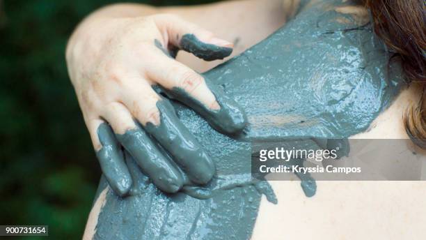woman applying volcanic mud treatment on shoulders - schlammbad stock-fotos und bilder