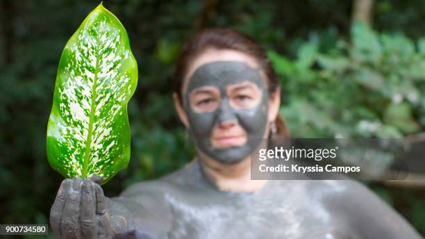 woman showing a rainforest leaf and using a mud facial mask - ollas de barro fotografías e imágenes de stock