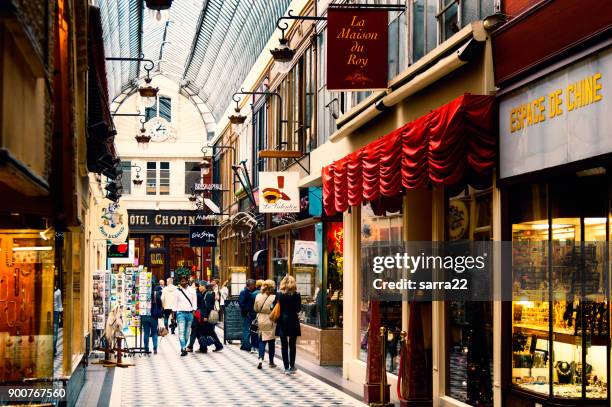 there are people, who are going shoping through passage jouffroy  - shopping area with clothing stores, book stores, jewelers shops, confectionery. - arcade stock pictures, royalty-free photos & images