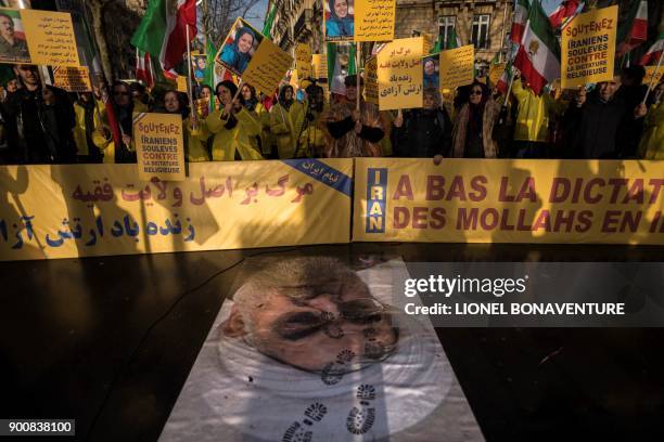 Protesters hold placards reading "Support Iranians risen up against the religious dictatorship" as they stand behind a portrait of Iranian President...