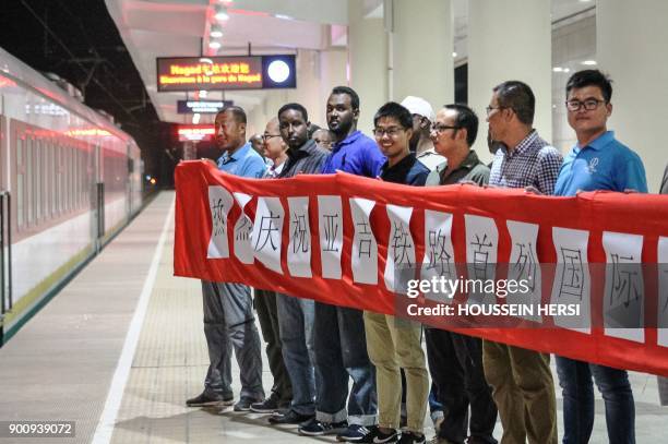 Workers of a Chinese construction company hold a banner to welcome the first commercial train as it arrives at a platform at Nagad railway station in...
