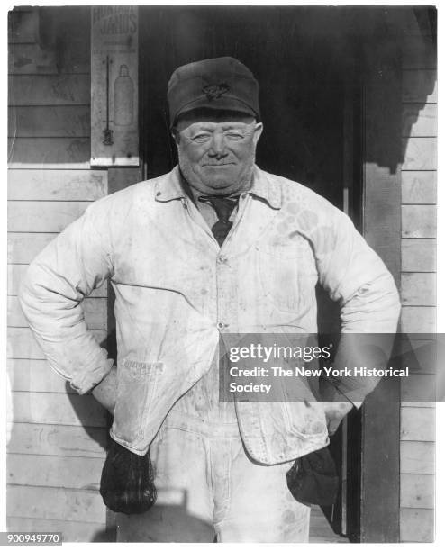 Stevedore Jerry Simpson standing in doorway in dirty work clothes, with weathered face, arms akimbo, 1907.