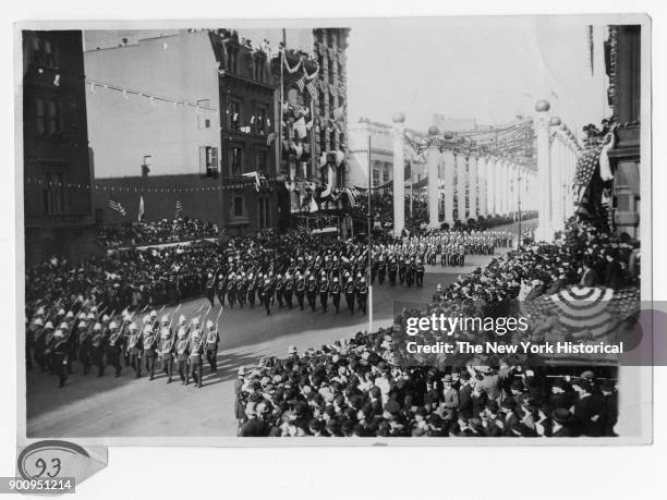 Military Parade at Court of Honor with military men with large hats, guns; crowds line street; large columns line street in background, 1909.