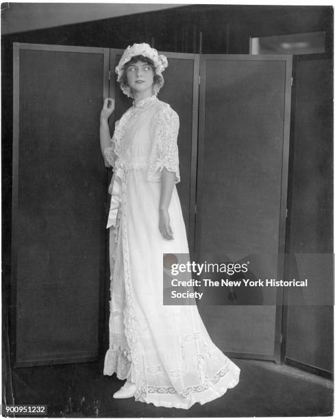 Model in front of screen, wearing lacey peignoir and nightcap, 1911.